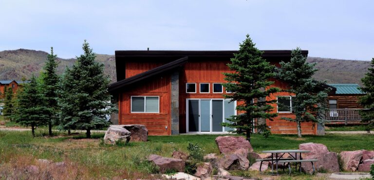 Luxury Mountain Cabin BackYard Showing Rock Garden, Large Green Grass Area, Cement Patio With BBQ. GLASS SLIDER DOOR entrance into stand-alone private family cabin.
