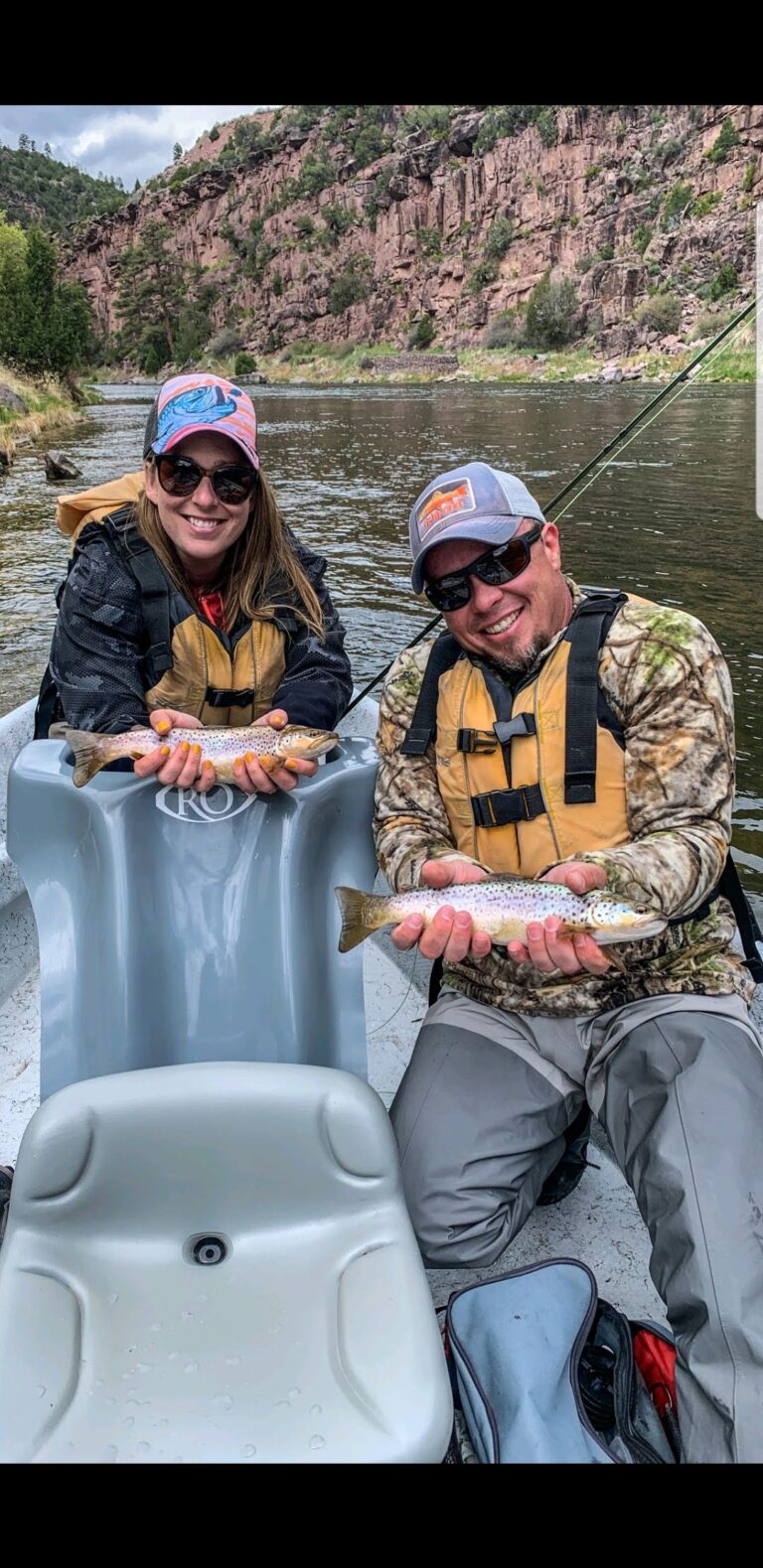 Husband and wife side by side in a green river fishing guide drift boat in Red Canyon releasing two wild brown trout into the green river by Dutch John resort